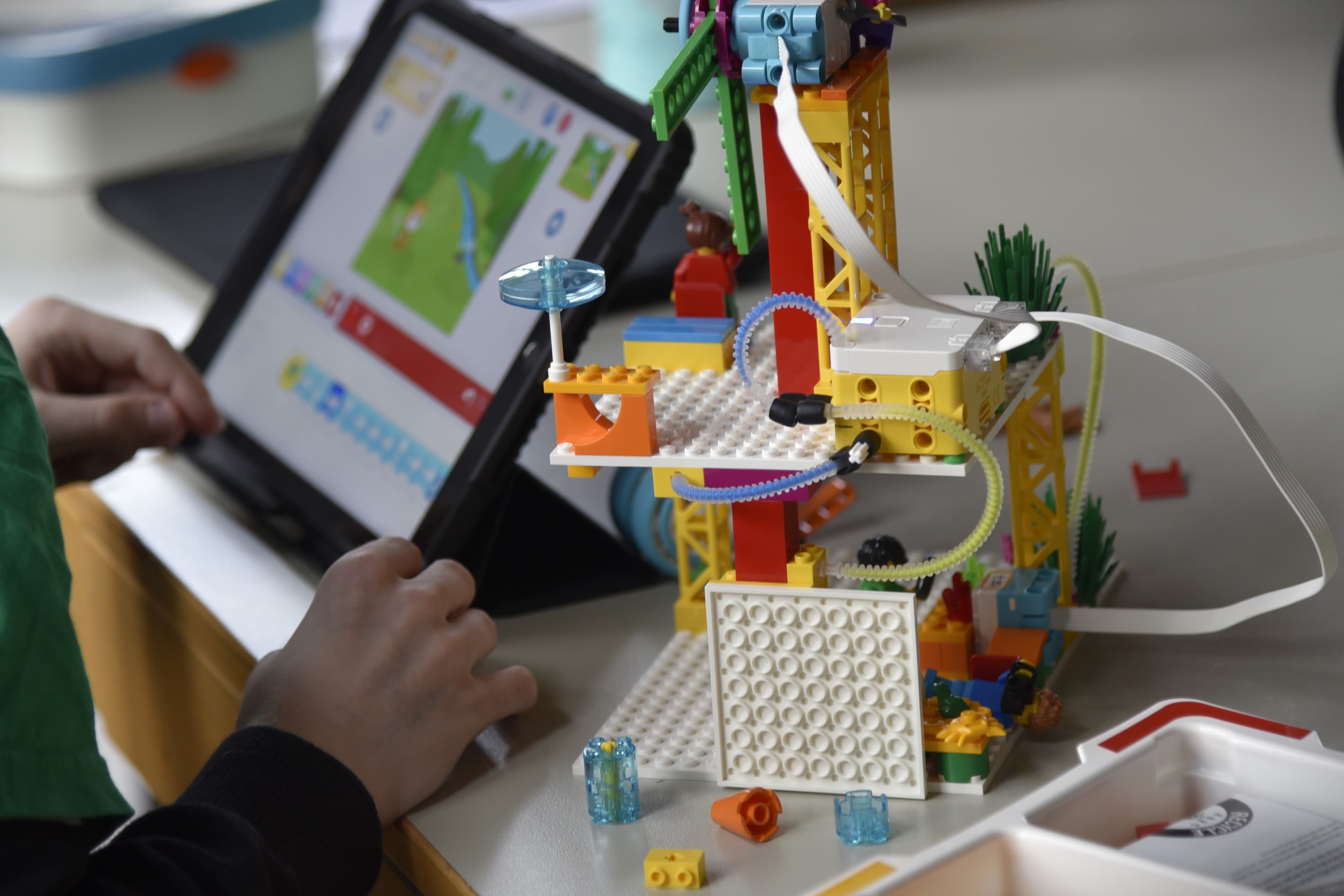 Eine Person sitzt vor einem Tablet. Davor ist ein gebautes Lego-Objekt zu sehen, was über das Tabelt gesteuert werden kann.