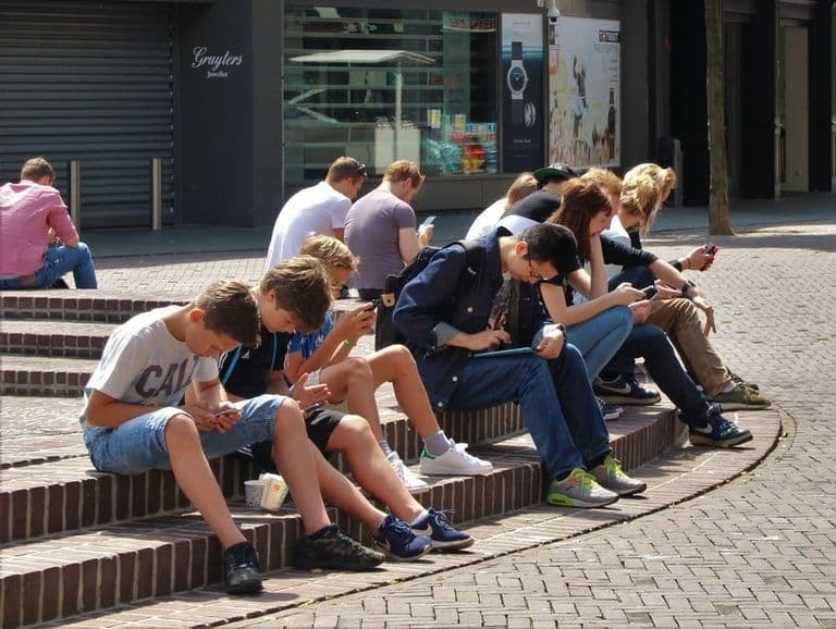 Zu sehen sind mehrere Jugendliche, die in ihre Smartphones vertieft sind.