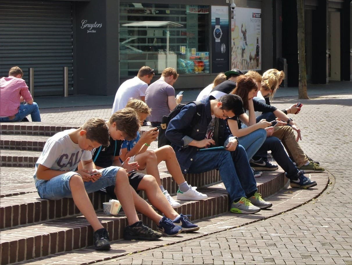 Zu sehen sind mehrere Jugendliche, die in ihre Smartphones vertieft sind.